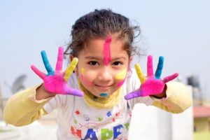 Asian child with multicolored paint on her hands and face